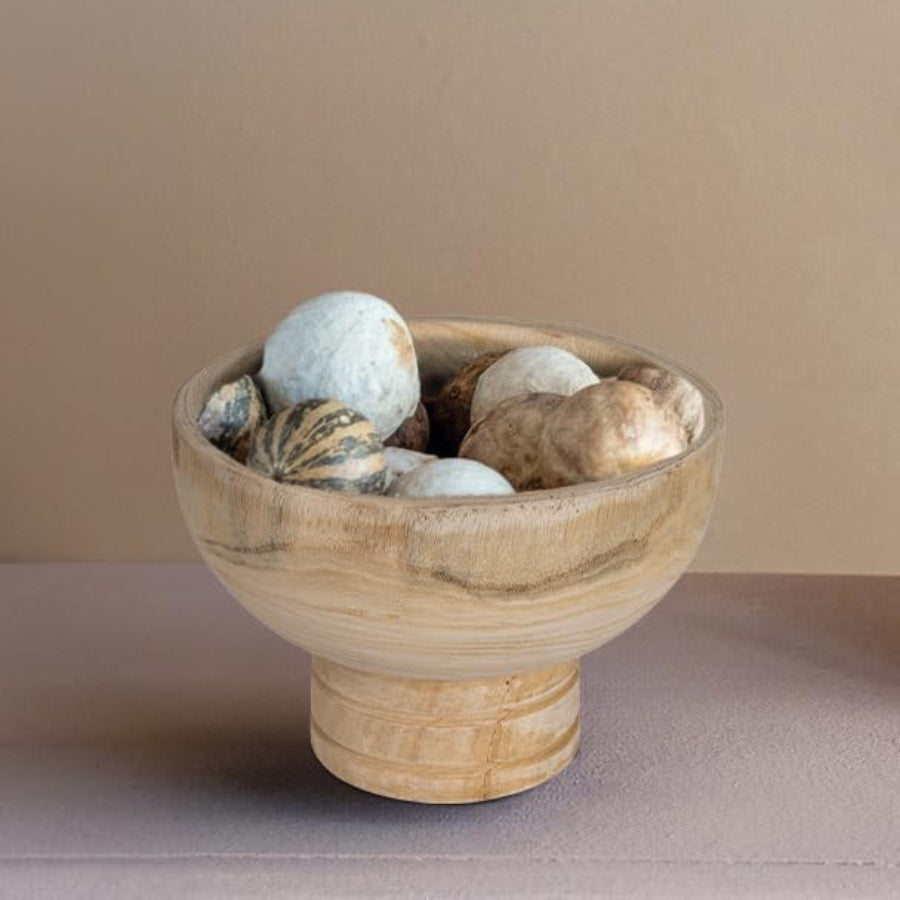 A natural paulownia wood pedestal bowl with a visible grain pattern with decor inside it